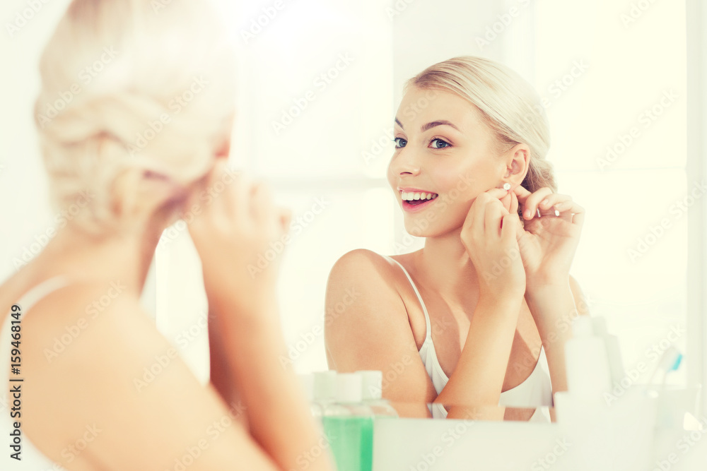 woman trying on earring looking at bathroom mirror woman trying on earring looking at bathroom mirror