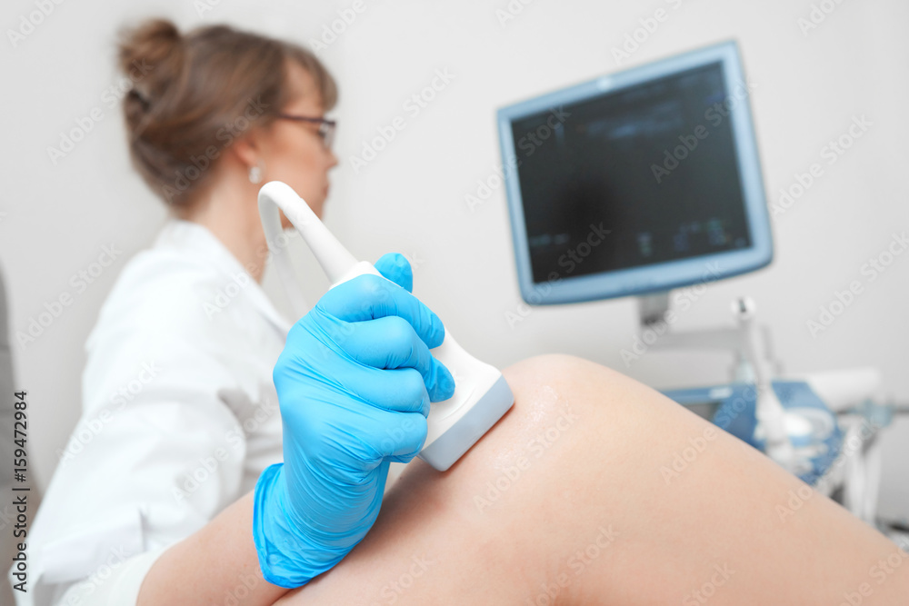 Cropped close up of a female doctor holding ultrasound scanner examining knee of her patient technology modern equipment medical treatment examination injury healthcare concept. Cropped close up of a female doctor holding ultrasound scanner examining knee of her patient technology modern equipment medical treatment examination injury healthcare concept.