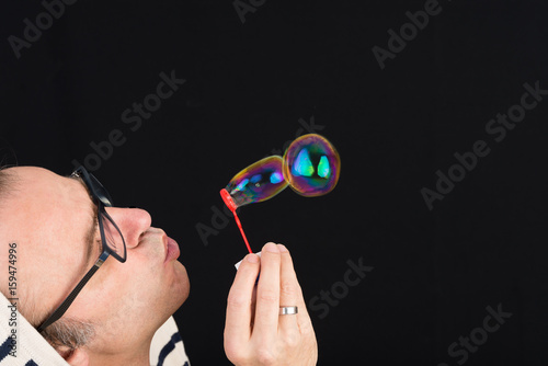 middle aged man blowing soap bubbles - studio shot against dark gray backgrouind photo