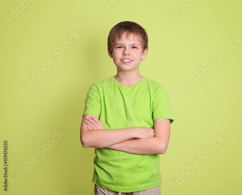 Confident preteen boy portrait with arms crossed isolated on green background.