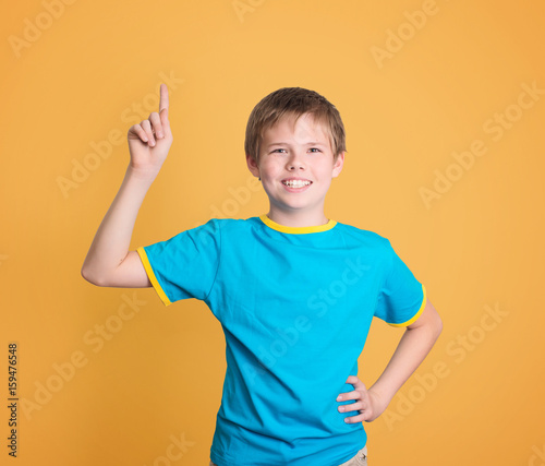 Happy child with good idea holds finger up isolated on yellow background