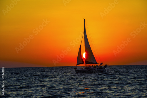 full sail sailing boat against ocean sunset