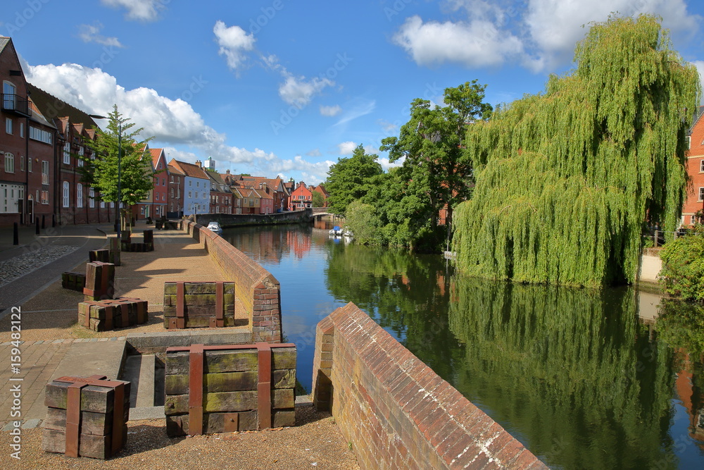 The riverside (river Wensum) in Norwich (Norfolk, UK) with colorful houses on the left side and the Fye Bridge in the background