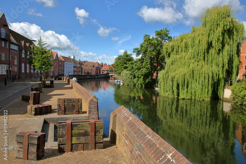 The riverside (river Wensum) in Norwich (Norfolk, UK) with colorful houses on the left side and the Fye Bridge in the background