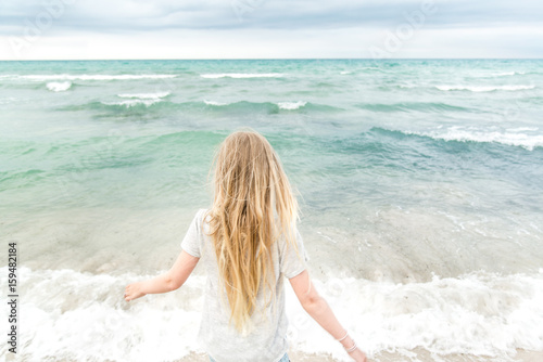 Young blonde girl standing on the beach © KariDesign