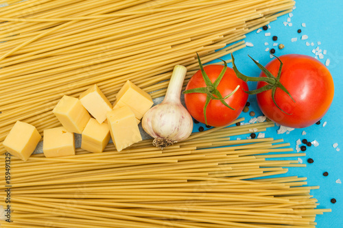 Top view of Italian ingredients of pasta and vegetables (tomatoes, pasta, garlic, pepper, cheese, spices) on a blue background.