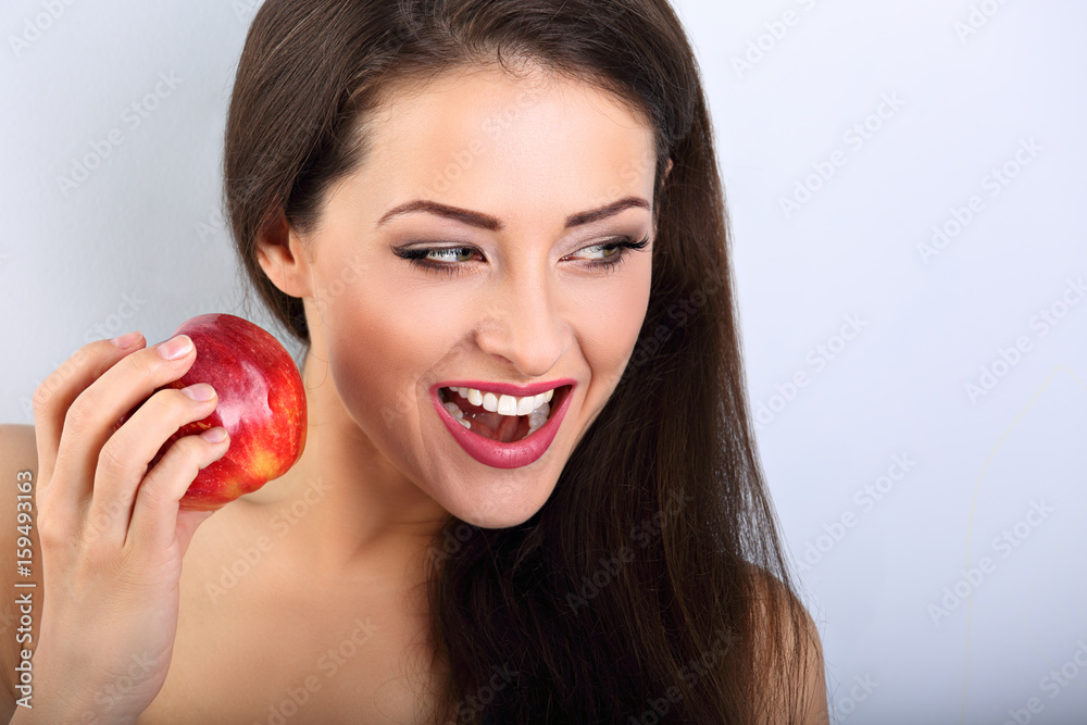 Beautiful excited makeup brunette woman holding red tasty apple and with open mouth looking on empty space blue background. Closeup portrait Beautiful excited makeup brunette woman holding red tasty apple and with open mouth looking on empty space blue background. Closeup portrait