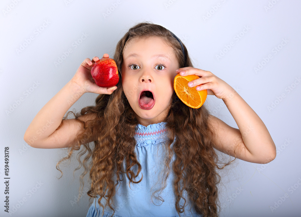 Joying humor grimacing happy kid girl with curly hair style holding citrus  orange fruit and red