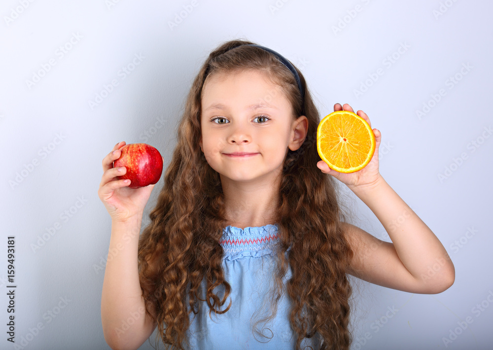 Cute joying smiling kid girl with curly hair style holding citrus orange  fruit and red apple in the hands on blue background Stock Photo | Adobe  Stock