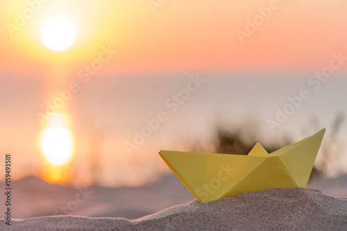 Yellow paper boat on a beach at sunrise