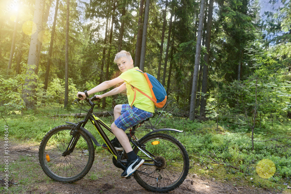 Happy teenager rides a bicycle in pine wood, in sunny day.