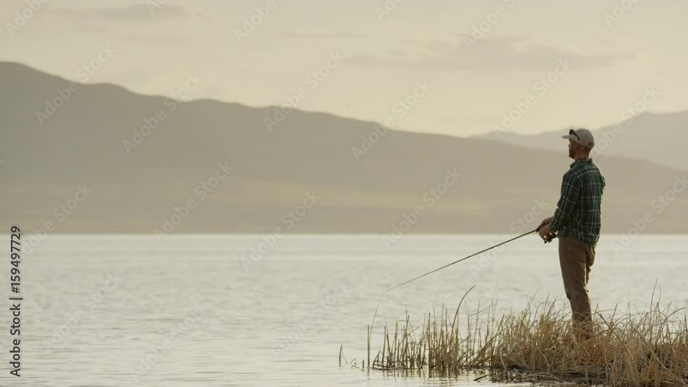 Wide panning shot of man fly fishing at lake. Vineyard, Utah, United States