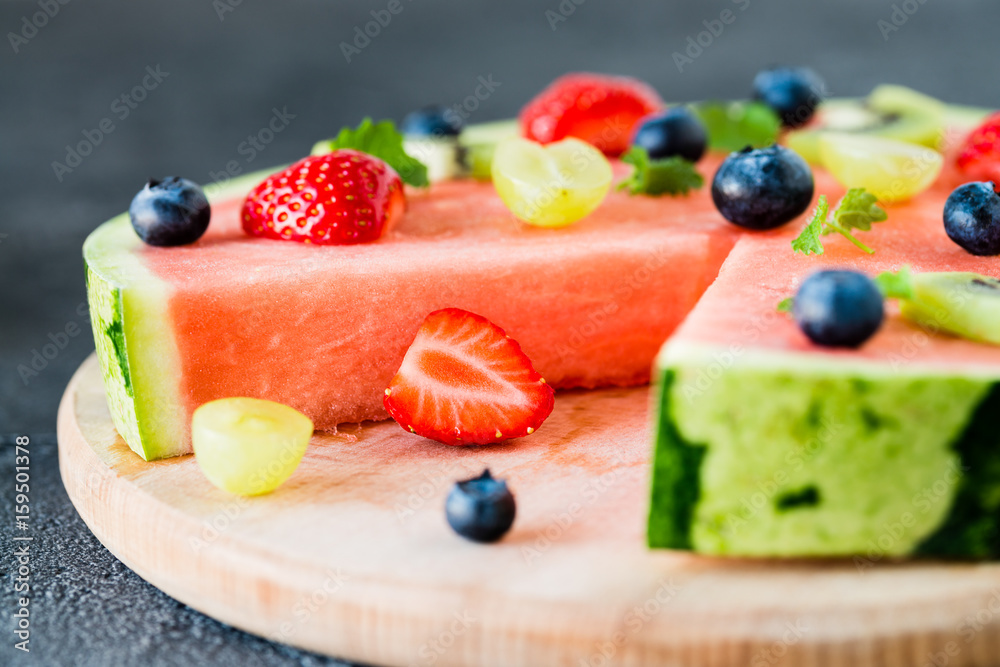 Watermelon pizza cut with fruits on wooden board, close up