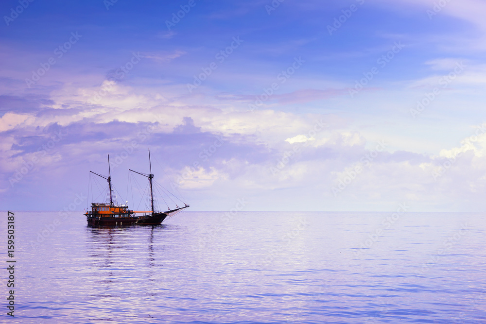 Wooden sailboat, or pinici, in vast Indian ocean under cloudy sky on sunrise, Indonesia. Seascape for wallpaper or background.