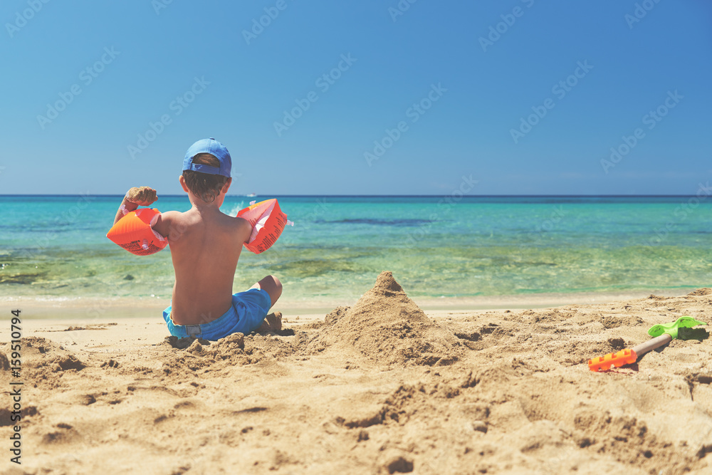 Boy in floating sleeves on a beach with transparent water. Boy in floating sleeves on a beach with transparent water.