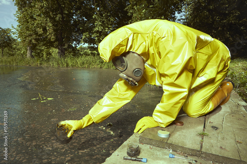 Man in chemical protective suit collecting samples of water contamination photo