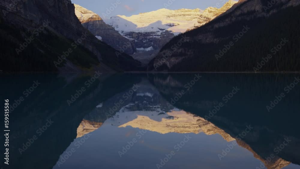 Wide tilting shot of reflection of mountains in still lake. Lake Louise, Alberta, Canada