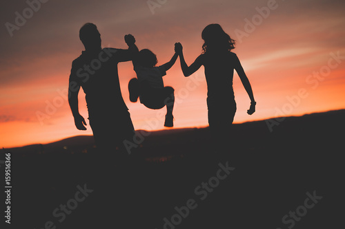 Mother and Father swinging son up in the air at sunset