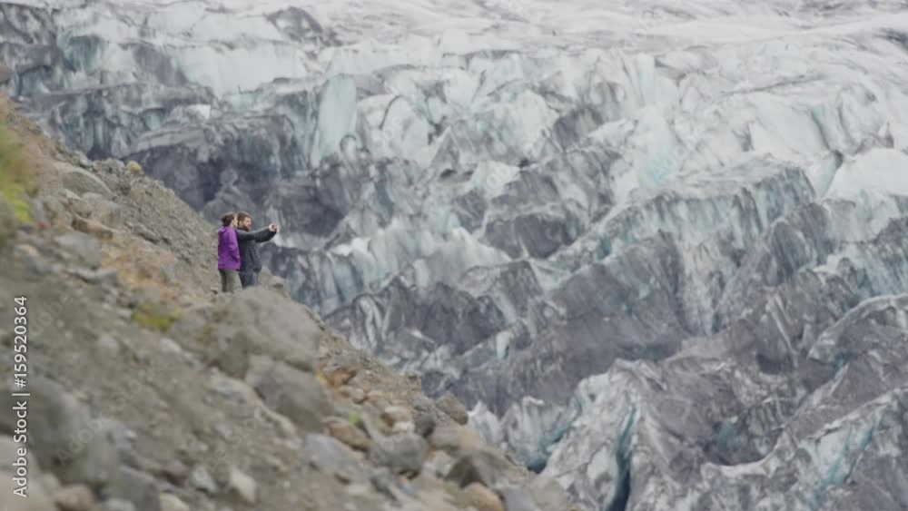 Wide shot of couple photographing ice on mountain range. Austur-Skaftafellssysla, Iceland Wide shot of couple photographing ice on mountain range. Austur-Skaftafellssysla, Iceland