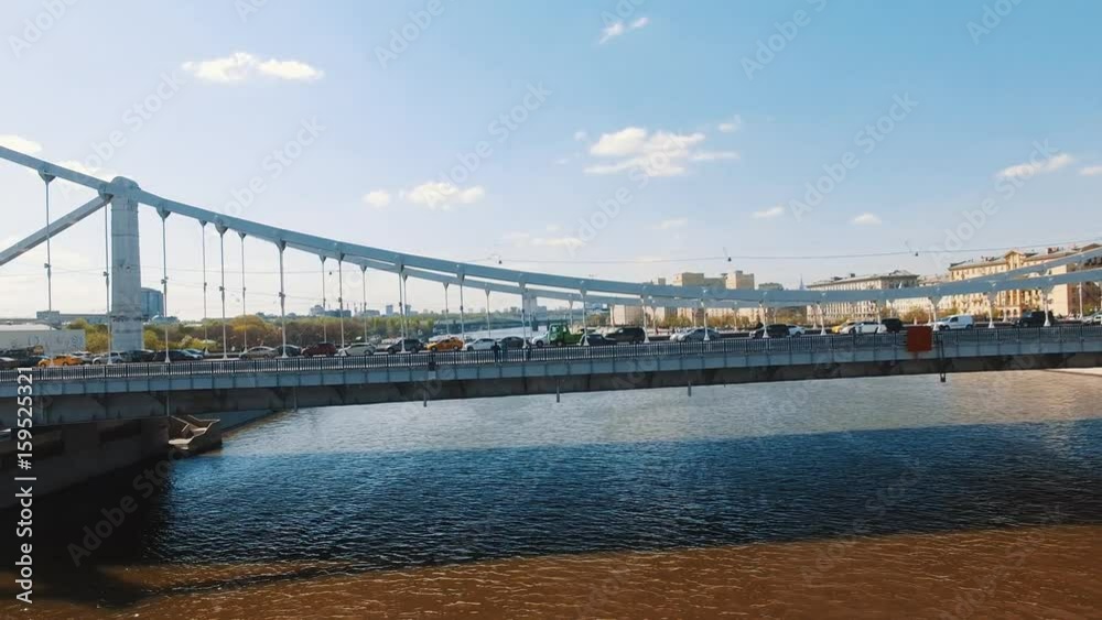 Drone shot of city river, road traffic on concrete bridge, boats in water trees park on shore, warm sunny summer day Drone shot of city river, road traffic on concrete bridge, boats in water trees park on shore, warm sunny summer day