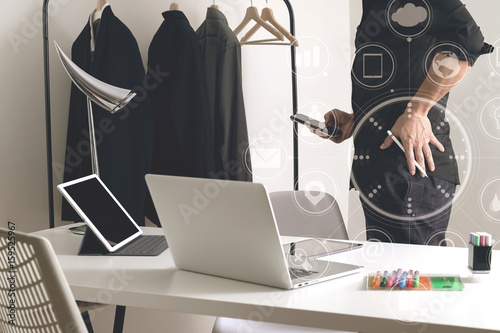 Fashion designer talking mobile phone and using laptop with digital tablet computer in modern studio