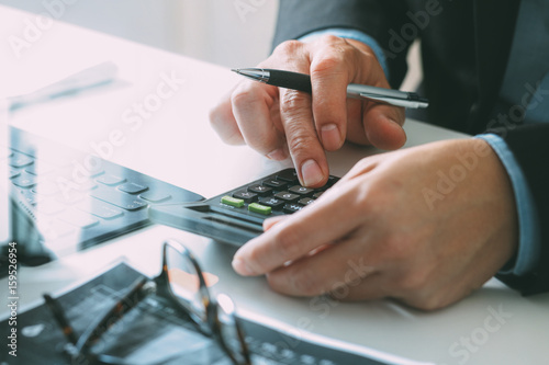 close up of businessman hand working with finances about cost and calculator and latop with mobile phone on withe desk in modern office