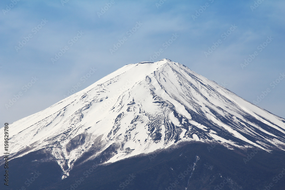 The peak of  Fuji mountain top filled with white snow and blue sky background.