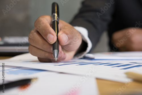 young successful man holding pen analyzing marketing graph in modern office. Businessman make a strategy plan at workplace. Business people working on table with financial chart