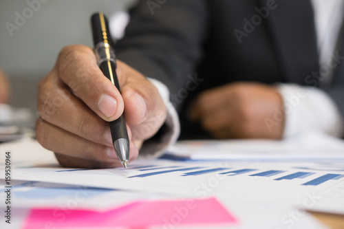 young successful man holding pen analyzing marketing graph in modern office. Businessman make a strategy plan at workplace. Business people working on table with financial chart