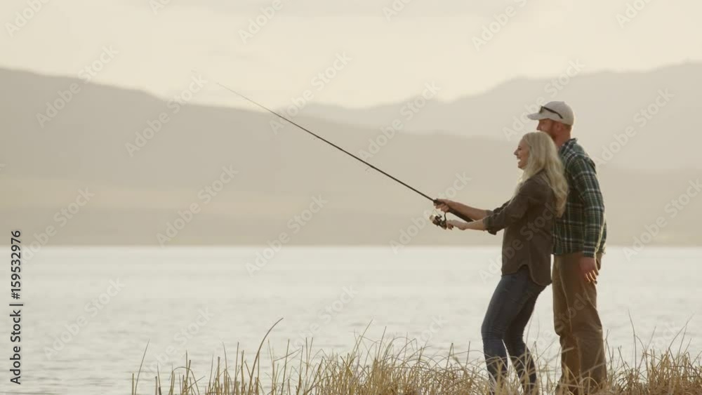 Wide panning shot of man watching woman fly fishing at lake. Vineyard, Utah, United States Wide panning shot of man watching woman fly fishing at lake. Vineyard, Utah, United States