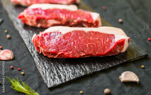 Fotografie New york strip porterhouse steak meat with spices and herbs against black backgr