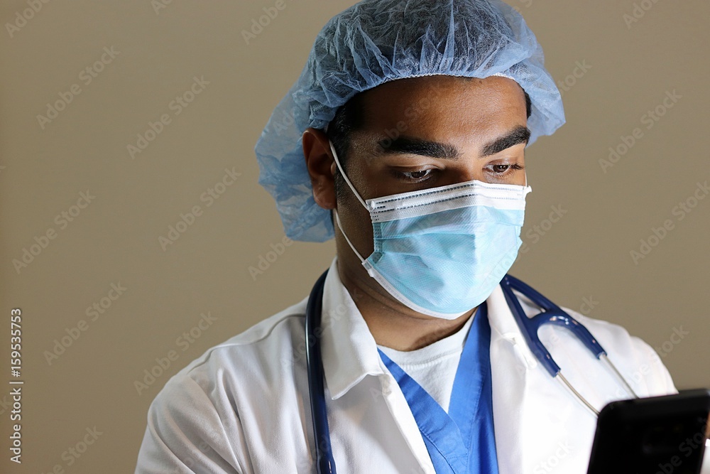 Young handsome doctor in blue scrubs looking at phone Young handsome doctor in blue scrubs looking at phone