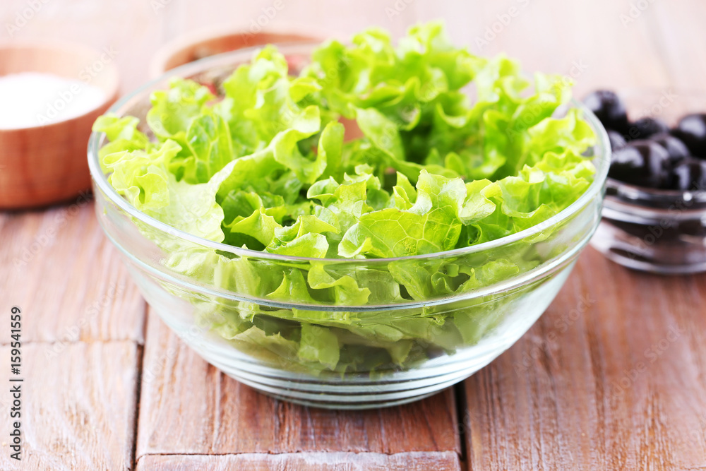 Green lettuce leafs in bowl on brown wooden table Green lettuce leafs in bowl on brown wooden table