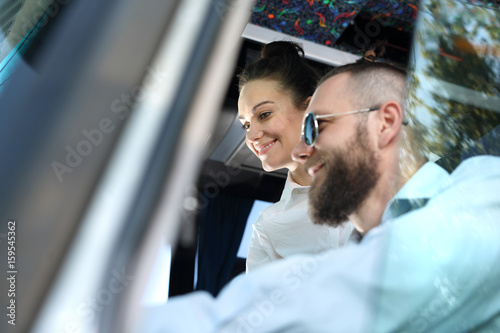 Kierowca autobusu kieruje pojazdem. Pasażerka autobusu rozmawia z kierowcą autobusu podczas postoju.