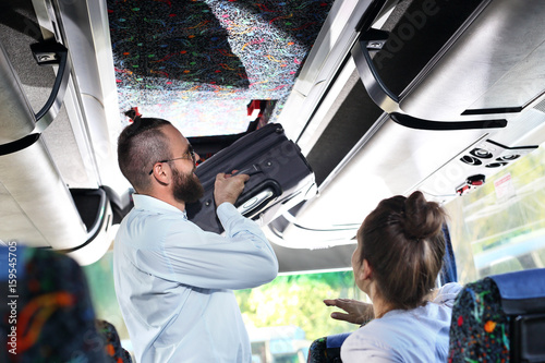 Bagaż podręczny. Kierowca autobusu turystycznego wkłada małą walizkę do luku bagażowego wewnątrz pojazdu.