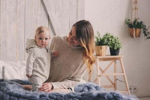 happy mother and 8 month old baby playing and relaxing at home in bedroom in the morning. Cozy family lifestyle in modern scandinavian interior.
