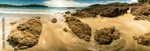 Panorama of a sandy beach with volcanic stones and turquoise sea in New Zealand photo