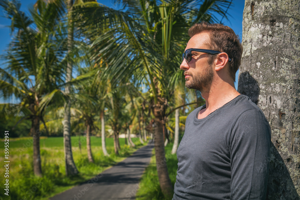 Man standing near empty road with palm trees.