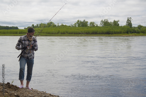 Fisherman in summer in a hat, shirt and jeans fishing for spinning on the bank of a mountain river