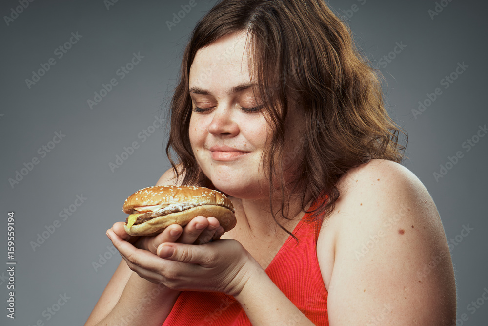 Hungry woman sniffing a hamburger on a gray background Hungry woman sniffing a hamburger on a gray background