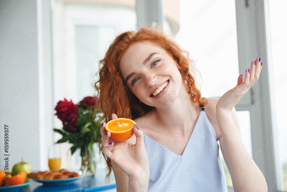 Cute happy young redhead lady near flowers holding orange Cute happy young redhead lady near flowers holding orange