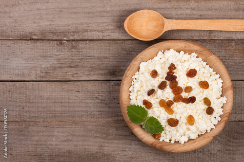 Cottage cheese with raisins in a wooden bowl on old wooden background with copy space for your text. Top view