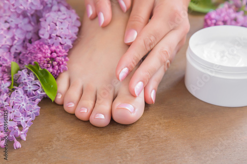Young woman's hands applying a foot moisturizing cream. Smooth skin. Spring and summer atmosphere with fresh, fragrant purple lilac flowers.