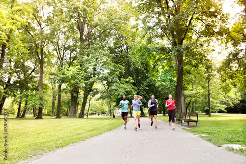 Group of young athletes running in green sunny park.