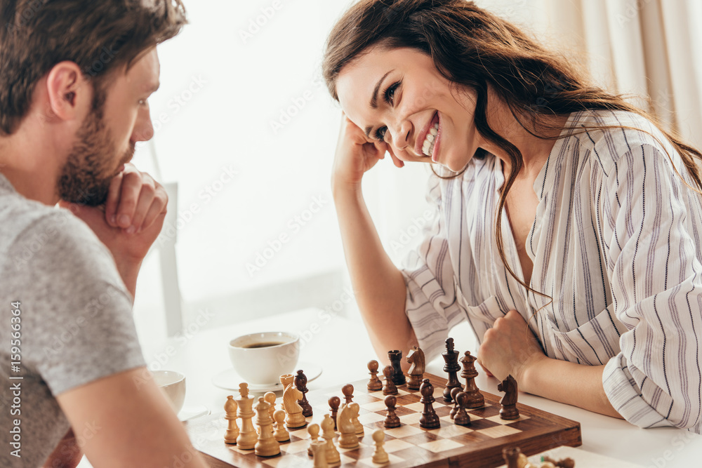 young couple playing chess while sitting at table at home young couple playing chess while sitting at table at home