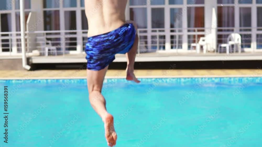 Back view of young athletic man in swim shorts running and jumping to the swimming pool. Slowmotion shot.