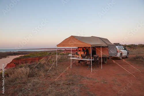 Man preparing a meal under awning of Off road camper trailer at sunset at James Price Point, Kimberley Australia photo