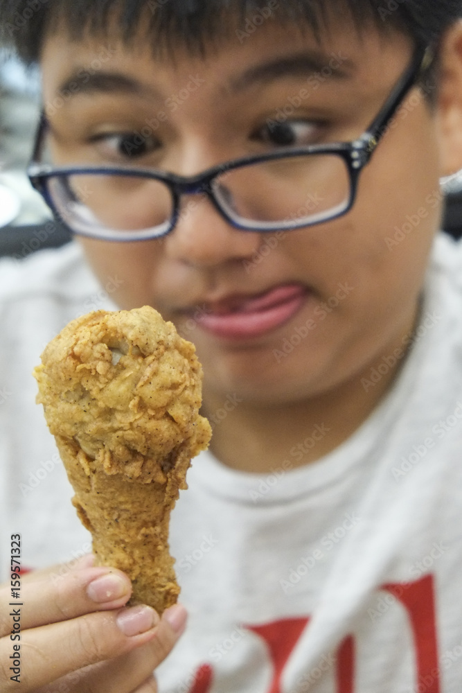 Hungry obese teenage kid licking lips and looking at fried chicken drumstick. Focus on chicken drumstick. Hungry obese teenage kid licking lips and looking at fried chicken drumstick. Focus on chicken drumstick.