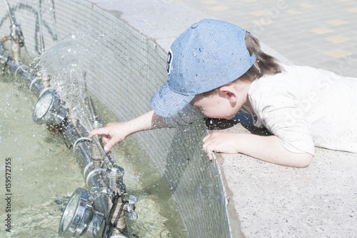A little boy in the city plays near the fountain with water