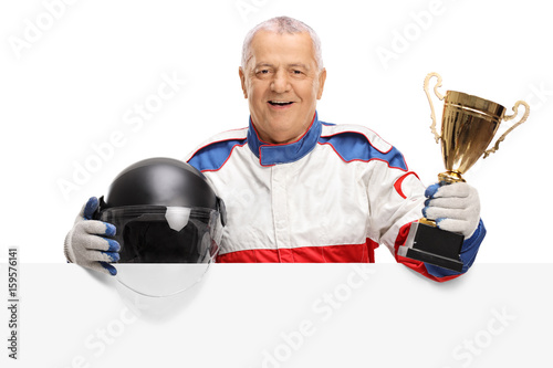 Mature car racer with golden trophy and helmet behind panel